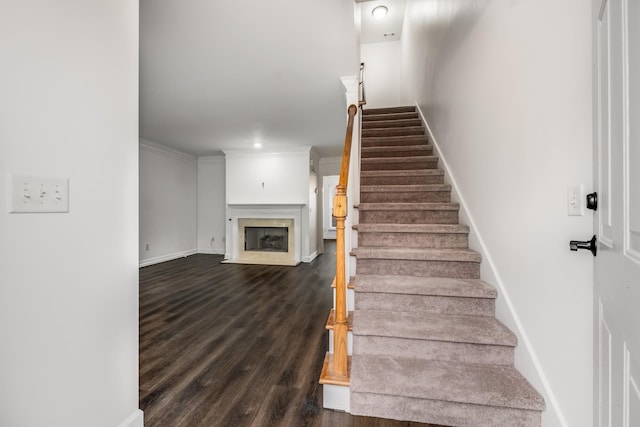 stairs featuring baseboards, ornamental molding, a fireplace with flush hearth, and wood finished floors
