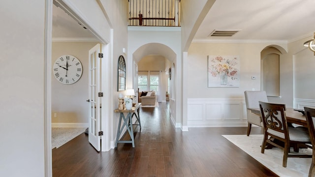 entryway with ornamental molding, wainscoting, visible vents, arched walkways, and dark wood-style floors