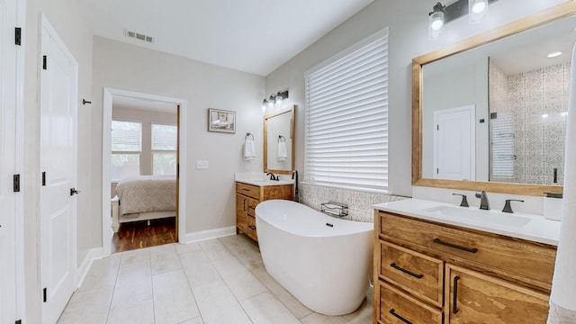 ensuite bathroom with a sink, two vanities, visible vents, and a freestanding tub