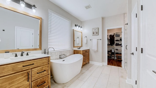 bathroom with two vanities, tile patterned floors, a freestanding tub, and a sink