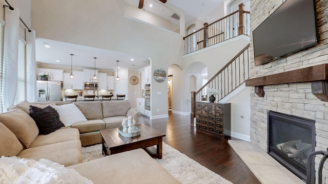 living room with a towering ceiling, arched walkways, a stone fireplace, and dark wood finished floors