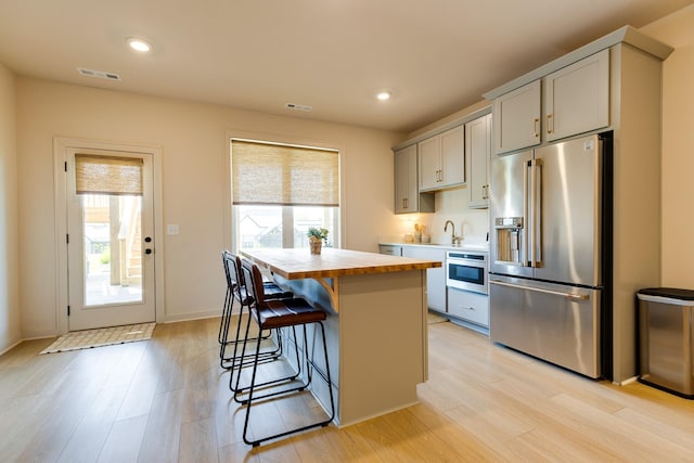 kitchen featuring light wood finished floors, stainless steel appliances, a kitchen breakfast bar, and butcher block countertops