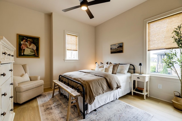 bedroom featuring multiple windows, a ceiling fan, light wood-style flooring, and baseboards
