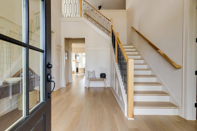 entrance foyer featuring stairway, light wood finished floors, a decorative wall, and a high ceiling