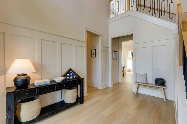 entryway featuring light wood finished floors, a decorative wall, and a towering ceiling