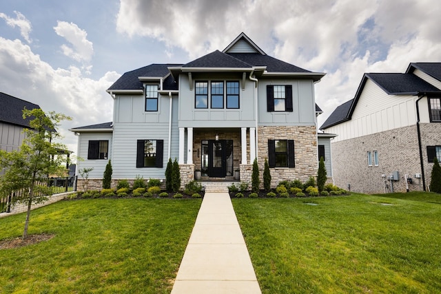 view of front of home with covered porch, stone siding, a front lawn, board and batten siding, and roof with shingles