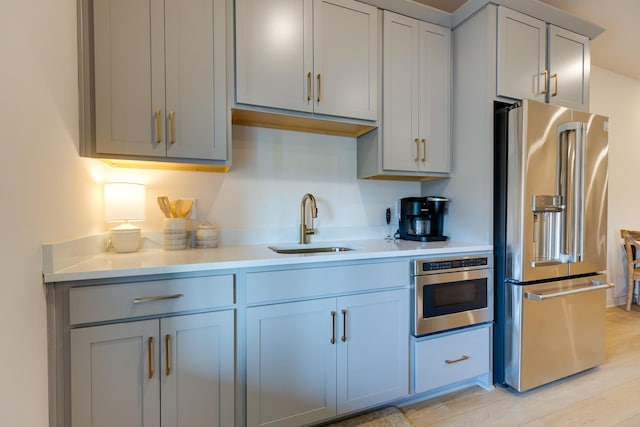 kitchen featuring a sink, stainless steel appliances, gray cabinets, light wood finished floors, and light countertops
