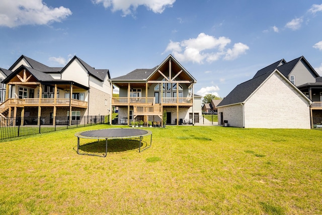 rear view of house with a trampoline, fence, and a lawn