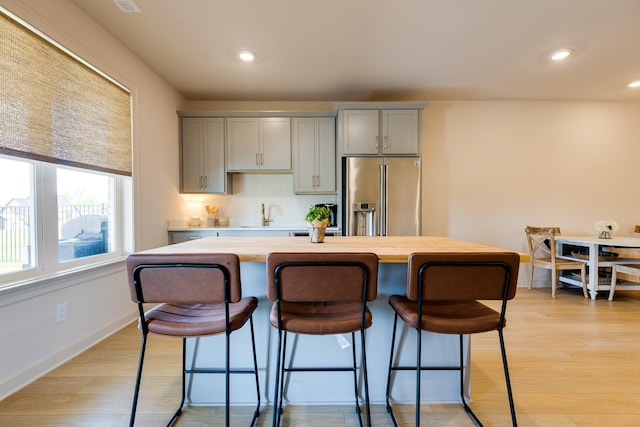 kitchen with light wood finished floors, a kitchen breakfast bar, gray cabinets, and high end fridge