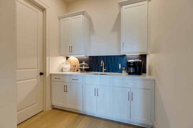 bar featuring light wood-type flooring, decorative backsplash, and a sink