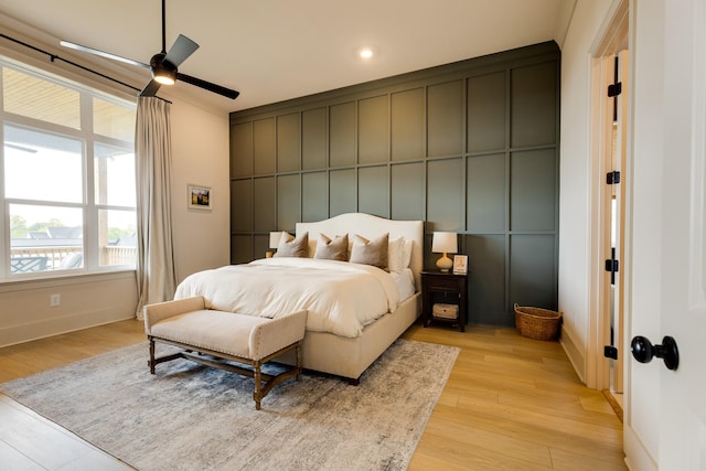 bedroom with ceiling fan, a decorative wall, light wood-type flooring, and baseboards