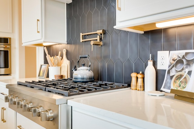 kitchen featuring stainless steel oven, range, light stone counters, backsplash, and white cabinets