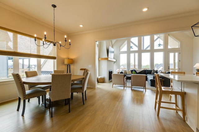 dining area featuring a fireplace, crown molding, light wood-style flooring, and a chandelier