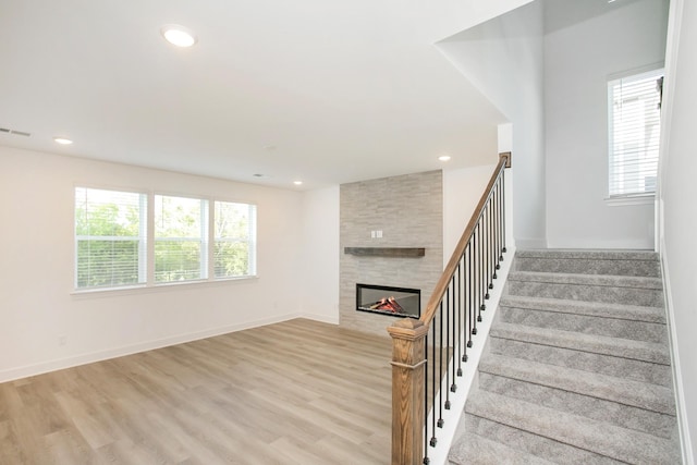 stairway featuring a tiled fireplace, plenty of natural light, and wood finished floors