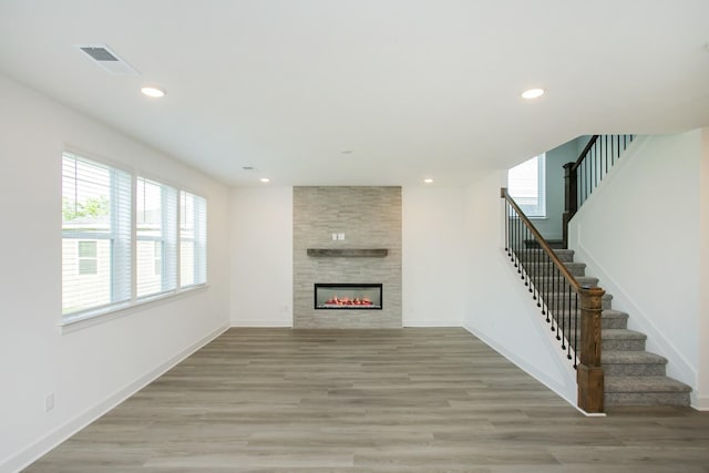 unfurnished living room with light wood finished floors, visible vents, a fireplace, and stairway