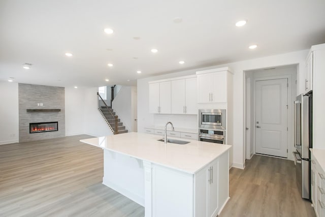 kitchen featuring a sink, appliances with stainless steel finishes, a kitchen island with sink, white cabinetry, and light wood-style floors