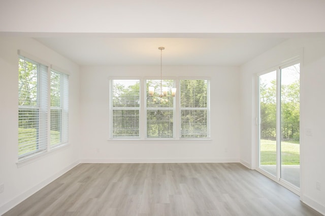 unfurnished dining area with baseboards, a notable chandelier, and light wood-type flooring