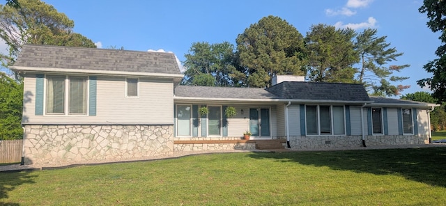 back of house with stone siding, a shingled roof, and a lawn