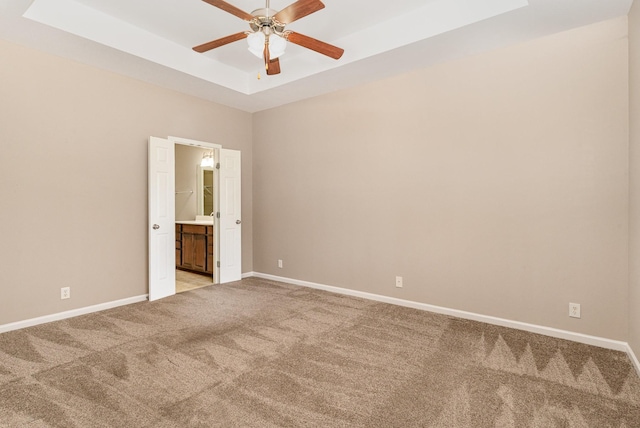 empty room with light colored carpet, baseboards, a ceiling fan, and a raised ceiling