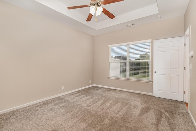spare room featuring a ceiling fan, a tray ceiling, baseboards, carpet flooring, and visible vents