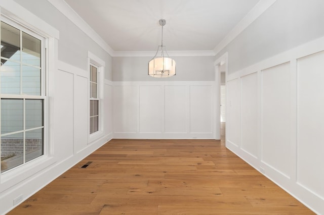 unfurnished dining area with light wood finished floors, a decorative wall, crown molding, a chandelier, and a wainscoted wall