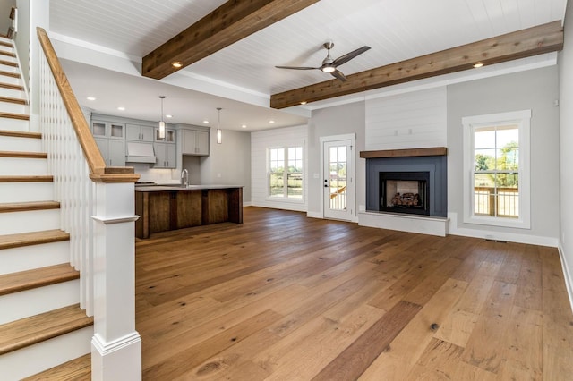 unfurnished living room featuring stairway, hardwood / wood-style flooring, ceiling fan, beamed ceiling, and recessed lighting