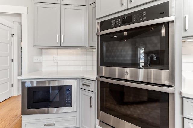 kitchen featuring built in microwave, stainless steel double oven, light countertops, light wood-style floors, and decorative backsplash