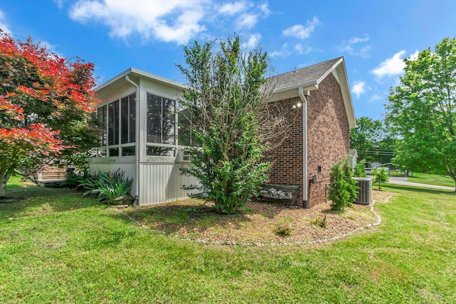 view of side of property with central air condition unit, a lawn, brick siding, and a sunroom