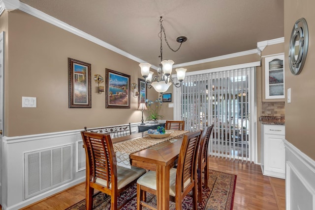 dining area featuring a chandelier, ornamental molding, light wood-type flooring, and wainscoting