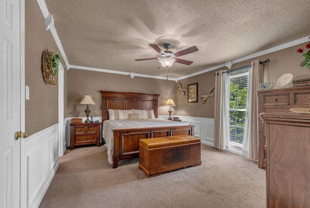 bedroom with ornamental molding, a wainscoted wall, light carpet, a textured ceiling, and a ceiling fan