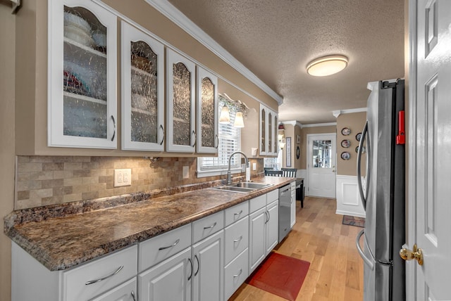 kitchen featuring stainless steel appliances, a sink, crown molding, a textured ceiling, and light wood-type flooring