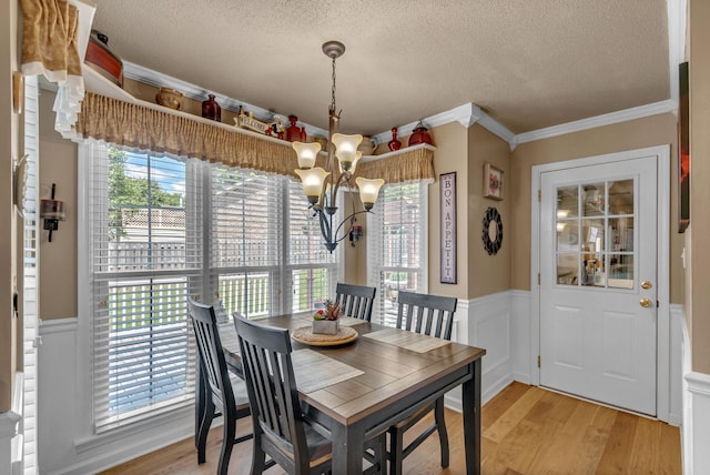 dining space with a chandelier, a textured ceiling, crown molding, a wainscoted wall, and light wood finished floors