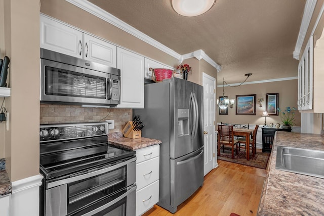 kitchen featuring appliances with stainless steel finishes, ornamental molding, white cabinets, decorative backsplash, and light wood-type flooring