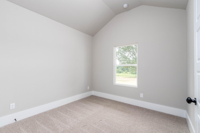 carpeted spare room featuring vaulted ceiling and baseboards
