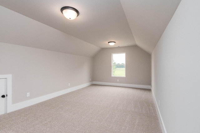 additional living space featuring baseboards, light carpet, and vaulted ceiling
