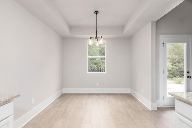 unfurnished dining area featuring light wood-type flooring, a chandelier, baseboards, and a raised ceiling