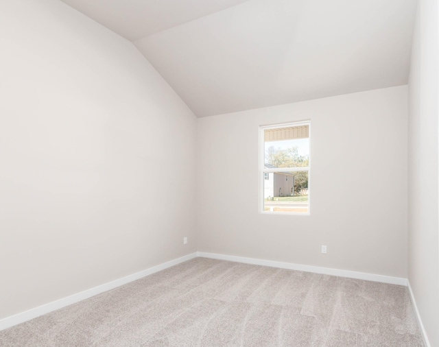 carpeted spare room with vaulted ceiling and baseboards