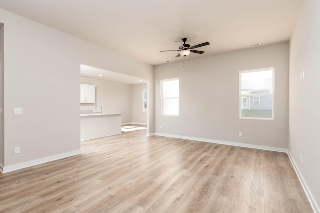 unfurnished living room with light wood-type flooring, baseboards, a ceiling fan, and a sink
