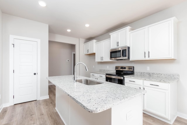 kitchen featuring light wood-style flooring, a sink, white cabinets, stainless steel appliances, and a kitchen island with sink