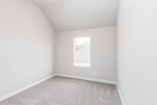 carpeted empty room featuring vaulted ceiling and baseboards