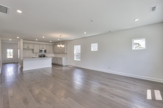 unfurnished living room with a notable chandelier, visible vents, a sink, and dark wood-type flooring