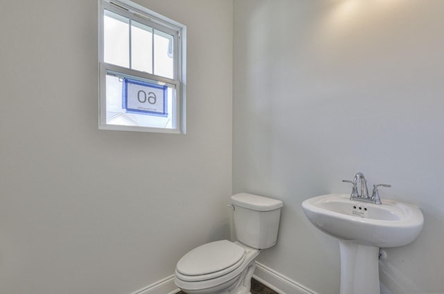 half bathroom featuring baseboards, toilet, and a sink