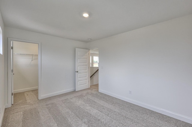 unfurnished bedroom with light colored carpet, a closet, baseboards, and a spacious closet