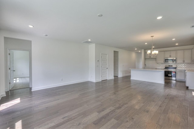 unfurnished living room with an inviting chandelier, wood finished floors, baseboards, and recessed lighting