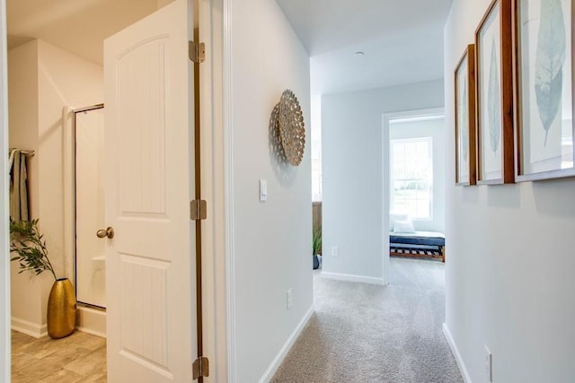corridor featuring baseboards and light colored carpet