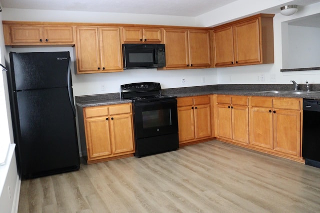 kitchen with a sink, dark countertops, brown cabinetry, black appliances, and light wood-style floors