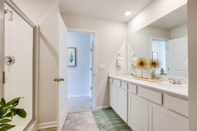 bathroom with double vanity, baseboards, a shower stall, and a sink