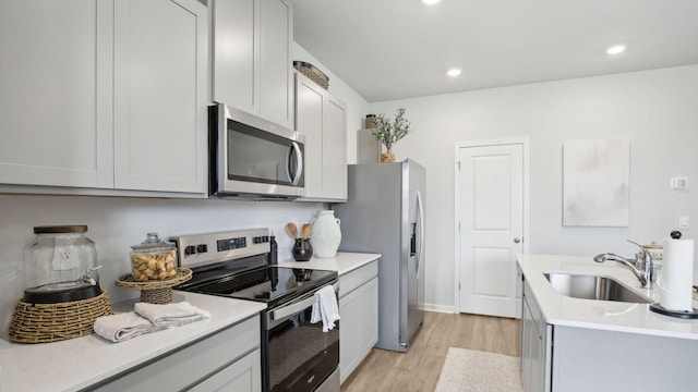 kitchen with a sink, recessed lighting, light wood-style flooring, light countertops, and appliances with stainless steel finishes