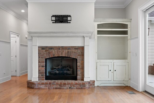 room details featuring baseboards, visible vents, a brick fireplace, crown molding, and wood finished floors