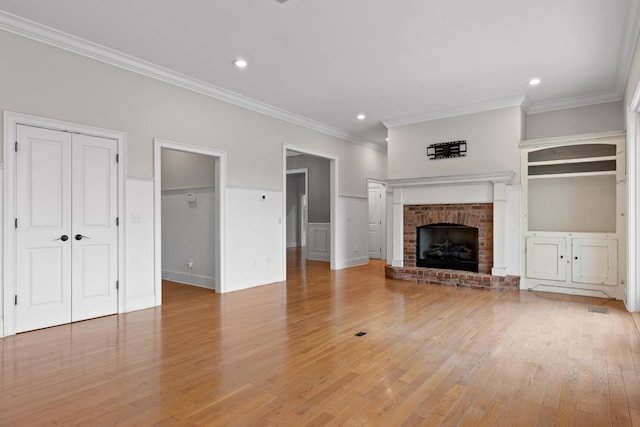 unfurnished living room featuring crown molding, recessed lighting, a brick fireplace, and light wood-style floors